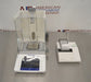 Top-down view of a Mettler Toledo XPE205 analytical balance resting on a stainless steel work surface, featuring its glass draft shield, internal weighing pan, front touchscreen terminal, and connected lab printer