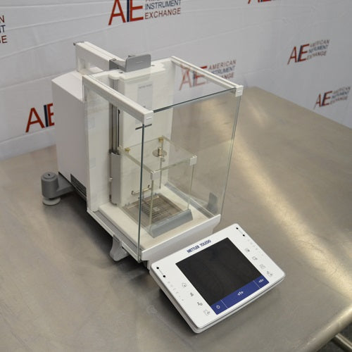 Angled perspective view of Mettler Toledo XPE26 microbalance showing glass draft shield enclosure, internal weighing chamber, rear housing, and front touchscreen control console