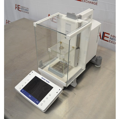 Left angled perspective view of Mettler Toledo XPE26 microbalance showing glass draft shield chamber, main housing, leveling feet, and touchscreen control unit