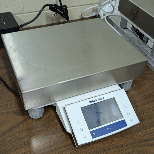 Front product view of a Mettler Toledo XS16001L digital precision balance, highlighting its large rectangular stainless steel weighing pan, leveling feet, and an attached front control terminal with a digital display screen