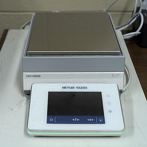 Front product view of a Mettler Toledo XSR10002S precision balance, showcasing the stainless steel weighing pan, digital touch terminal display, and housing on a workbench