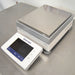 Left angled perspective view of a Mettler Toledo XSR6002S Excellence precision toploading balance on a stainless steel surface, featuring its rectangular stainless steel weighing pan, grey and white housing, and the angled front digital touchscreen terminal