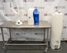 Front eye-level view of a Millipore Milli-Q Integral 15 water purification system featuring its main unit on a stainless steel table, remote dispensing arm, and a large storage reservoir tank