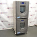 Left three-quarter angle product view of a New Brunswick Innova 42R stacked refrigerated incubator shaker system, showcasing the dual stacked grey chassis units, curved doors with central viewing windows, digital displays, and adjustable leveling feet