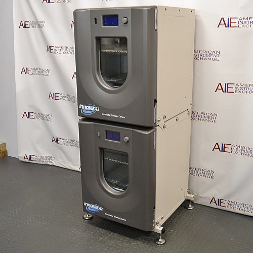 Right three-quarter angle product view of a New Brunswick Innova 42R stacked refrigerated incubator shaker system, showcasing the dual stacked grey chassis units, side panels, curved doors with central viewing windows, digital displays, and adjustable leveling feet