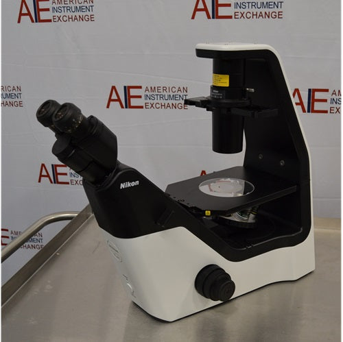 Right angled perspective view of a Nikon Eclipse Ts2 inverted microscope resting on a stainless steel surface, highlighting its modern black-and-white housing design, stage assembly, coarse focus knobs, overhead condenser tower, and binocular eyepieces