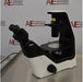 Right angled perspective view of a Nikon Eclipse Ts2 inverted microscope resting on a stainless steel surface, highlighting its modern black-and-white housing design, stage assembly, coarse focus knobs, overhead condenser tower, and binocular eyepieces