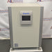 Studio front product view of a Panasonic Cell-IQ Series MCO-170AICUVL-PA CO2 cell culture incubator against a branded backdrop, highlighting its off-white outer cabinet, vertical silver side pillars, and central door-mounted digital touchscreen display featuring Panasonic branding