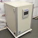 Studio three-quarter angle product view of a Panasonic Cell-IQ Series MCO-170AICUVL-PA CO2 cell culture incubator against a branded backdrop, highlighting its off-white body, heavy-duty side hinges, vertical silver corner trims, central Panasonic touchscreen interface, and wheeled platform base