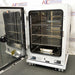 Studio angle product view of a PHCBi Cell-IQ Series CO2 laboratory incubator with the outer door swung open against a branded backdrop, highlighting its white housing, heavy door hinges, open inner chamber with multiple stainless steel wire shelves, a lower water pan, and wheeled base platform