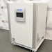 Studio right three-quarter angle product view of a PHCBi Cell-IQ Series CO2 laboratory incubator against a branded backdrop, highlighting its white outer body, vertical silver corner pillars, central door-mounted digital touchscreen interface, right side panel labels, and mobile roller base
