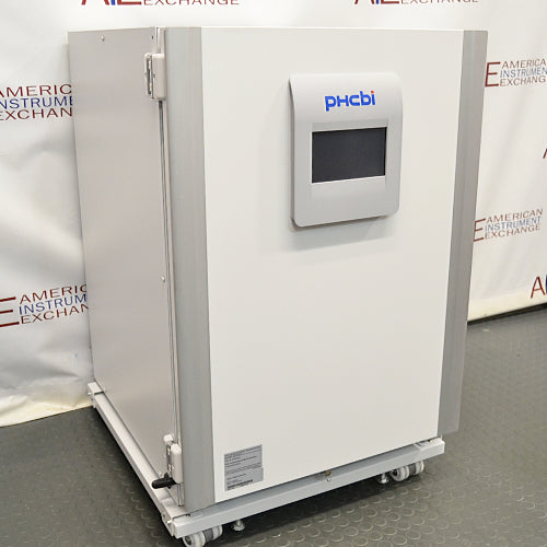 Studio three-quarter angle product view of a PHCBi Cell-IQ Series CO2 laboratory incubator against a branded backdrop, highlighting its large white outer cabinet, heavy-duty door hinges on the side, vertical silver pillars, central touchscreen display, and wheeled base platform
