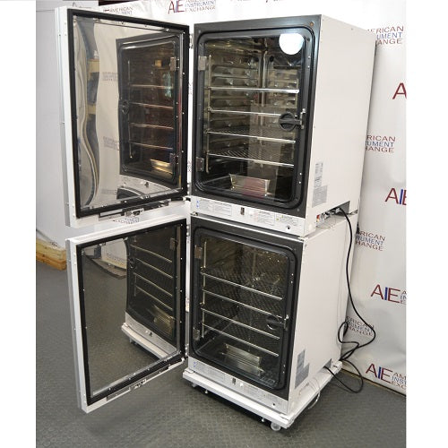 Left angled perspective view of stacked PHCbi Cell-IQ Series high heat sterilization CO2 incubators with outer and inner glass doors open showing stainless steel interior shelves