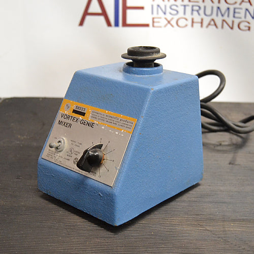 Left three-quarter angle product view of an S/P Scientific Products Vortex-Genie mixer, showing its blue cast housing, top rubber mixing head, control faceplate, and power cord on a dark workbench
