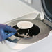 Close-up view of a Sartorius LMA200 microwave moisture analyzer in use, with a gloved hand holding tweezers to place a sample filter paper onto the holder inside the open microwave heating chamber