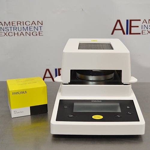 Front product view of a Sartorius MA35 infrared moisture analyzer accompanied by a box of Sartorius sample pans, featuring the white and black housing, digital control panel, and heating chamber