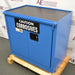 Left three-quarter angle product view of an unused Securall 24-gallon corrosive storage cabinet, focusing on the blue side panel, warning label, and secure door latch mechanism on a wood pallet