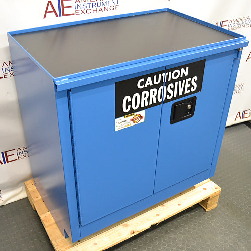Three-quarter angle product view of an unused Securall 24-gallon corrosive storage cabinet, showcasing the blue exterior finish, top containment tray surface, and warning label on a wooden shipping pallet