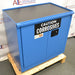 Three-quarter angle product view of an unused Securall 24-gallon corrosive storage cabinet, showcasing the blue exterior finish, top containment tray surface, and warning label on a wooden shipping pallet