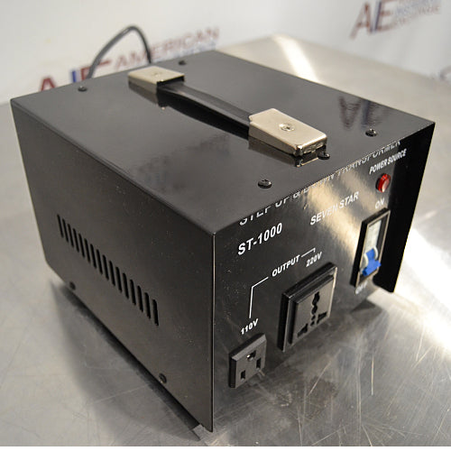 Left three-quarter angle product view of a Seven Star ST-1000 step up and down voltage transformer, showcasing the side ventilation slots, top handle, front faceplate with 110V and 220V output sockets, and power switch on a lab bench