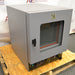 Front angled perspective view of a Shel Lab 1445 vacuum oven resting on a wooden pallet, highlighting its grey housing, glass viewing door with a latch handle, and lower control panel