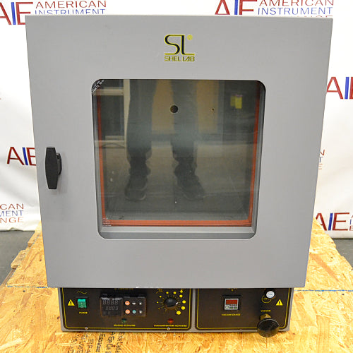 Front eye-level view of a Shel Lab 1445 vacuum oven resting on a wooden pallet, featuring a grey exterior, a glass viewing door with a latch handle, and a bottom control console with digital displays and switches