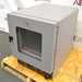 Right angled perspective view of a Shel Lab 1445 vacuum oven resting on a wooden pallet, highlighting its grey housing, glass viewing door with a latch handle, exterior door hinges, and lower control panel