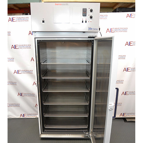 Thermo Forma 3920 environmental chamber ka open front view, jisme khula hua insulated door, multiple stainless steel wire shelves, interior chamber walls, aur top digital control panel saaf dikhai de rahe hain.   