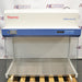 Front product view of a Thermo Scientific HeraGuard ECO 1.2 laminar flow clean bench, showcasing its white and blue housing, digital control panel, stainless steel work surface, and glass side walls on a wooden pallet