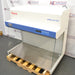 High-angle three-quarter product view of a Thermo Scientific HeraGuard ECO 1.2 laminar flow clean bench, showcasing its white housing, blue control console, stainless steel work deck, and glass panels on a wooden pallet