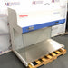 Right three-quarter angle product view of a Thermo Scientific HeraGuard ECO 1.2 laminar flow clean bench, featuring its white and blue exterior, digital control panel, stainless steel work deck, and glass side panels on a wooden pallet