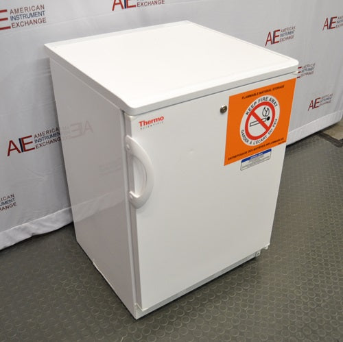 Three-quarter high-angle perspective view of a white Thermo Scientific undercounter flammable material storage refrigerator showing the top, side, and front door with a warning label
