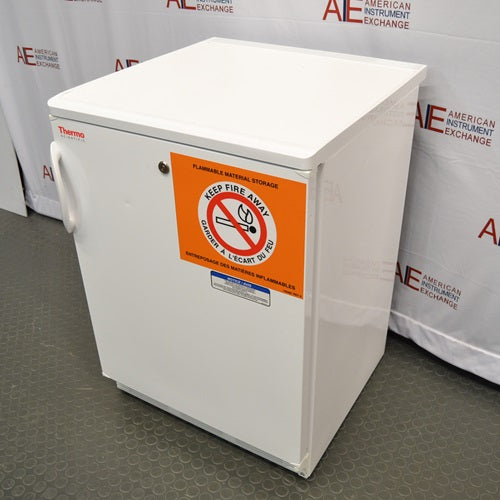 Three-quarter side perspective view of a white Thermo Scientific undercounter flammable material storage unit showing the front door handle and safety warning label