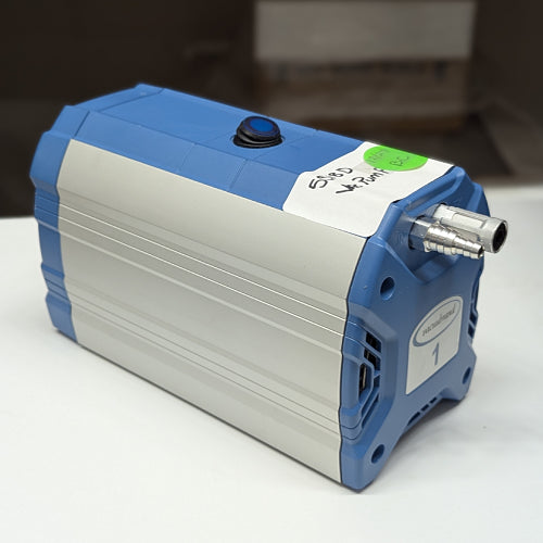 Right angled perspective view of a Vacuubrand ME1 diaphragm vacuum pump on a white surface, showcasing its compact rectangular housing with blue end caps, a top power switch, labeled asset tape, and front hose barb connection ports