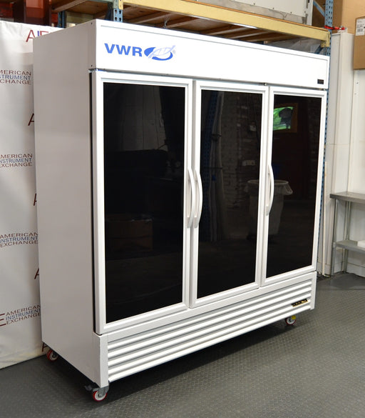 Front angled perspective view of a VWR triple glass door laboratory refrigerator on caster wheels, featuring a white exterior cabinet, three tinted glass doors with vertical handles, blue branding, and a louvered bottom grill panel