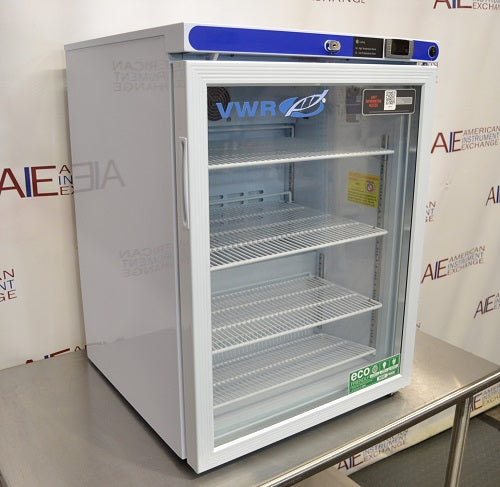 Angled perspective view of a VWR undercounter glass door laboratory refrigerator resting on a stainless steel surface showcasing its door handle, glass front, and top control console