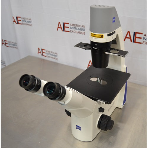 Front angled view of Zeiss Primovert inverted microscope featuring binocular viewing eyepieces, black specimen stage, focusing knob, and overhead illumination column
