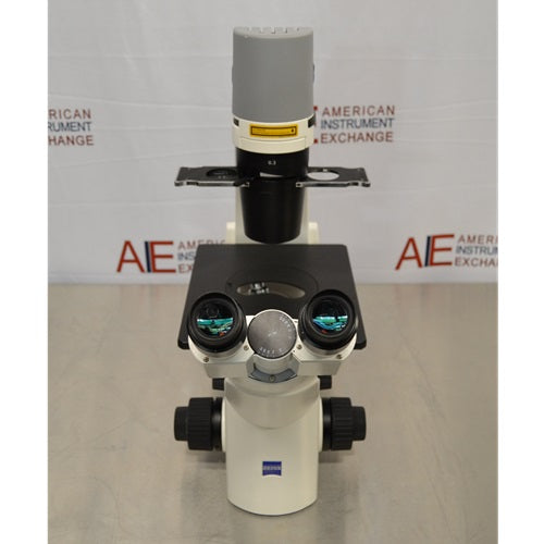 Slight high-angle front view of Zeiss Primovert inverted microscope showing binocular eyepieces, black specimen stage platform, slider condenser mount, and vertical condenser arm