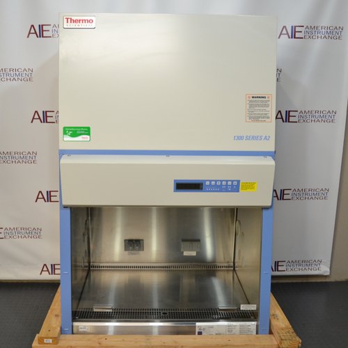 A front-facing view of a Thermo Scientific 1342 biosafety cabinet resting on a wooden pallet, showing its stainless steel interior workspace, digital control display panel, and blue and white exterior housing.